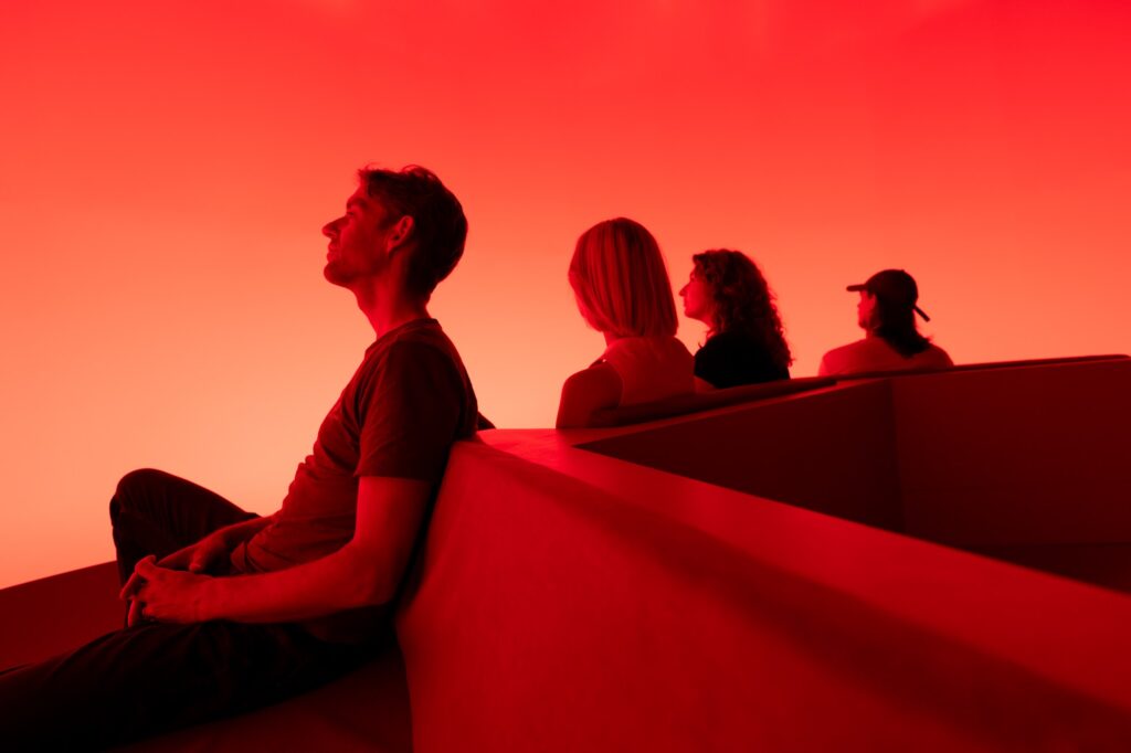 Visitors seated inside Chasing the Dot, bathed in orange-red light