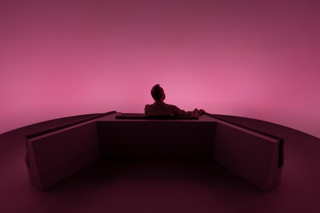 A lone visitor seated in soft mauve light inside Chasing the Dot