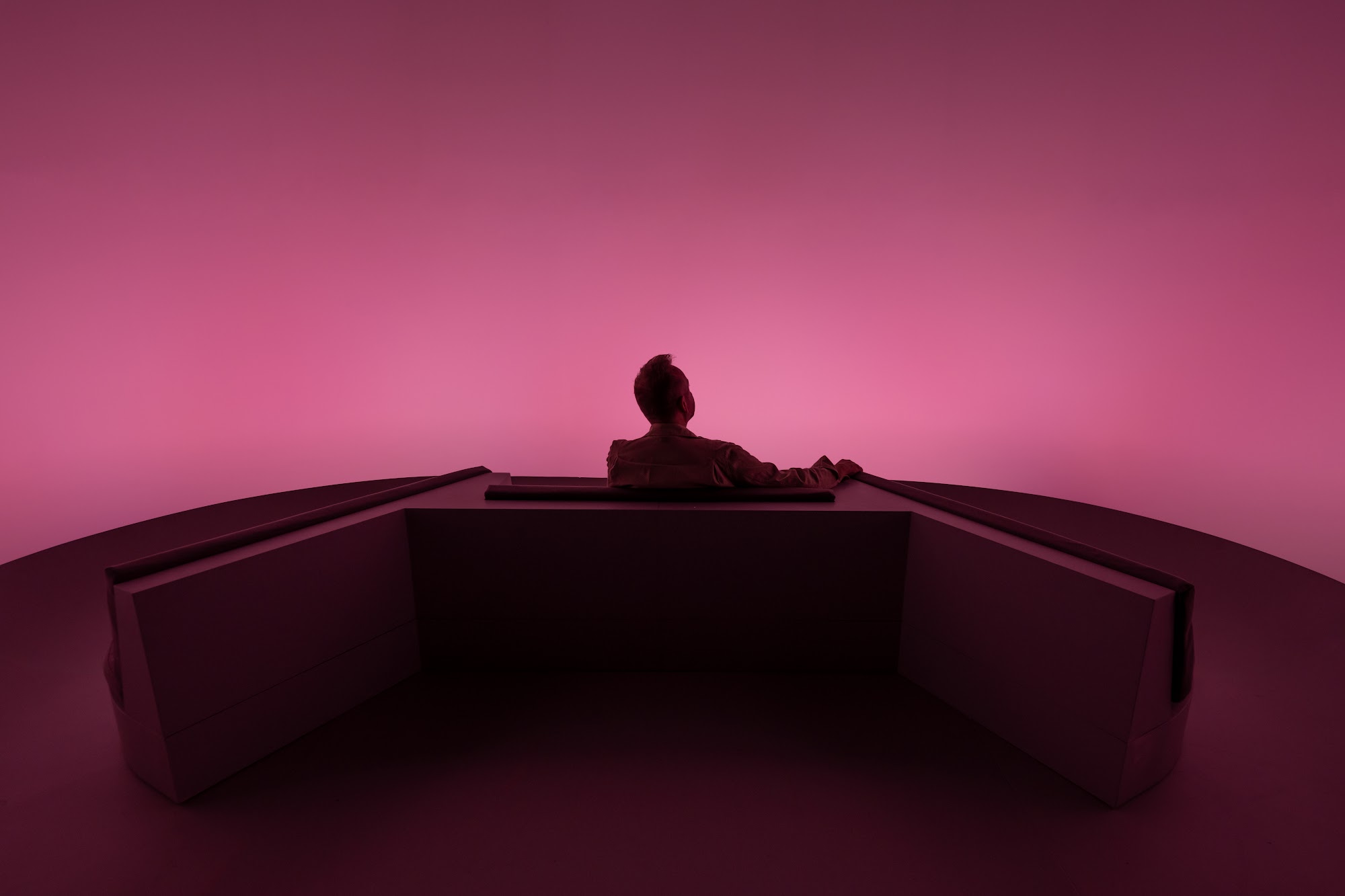 A lone visitor seated in soft mauve light inside Chasing the Dot