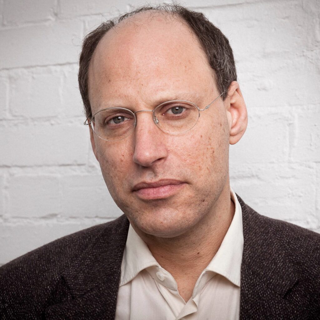 Portrait of Darian Leader against a white brick wall