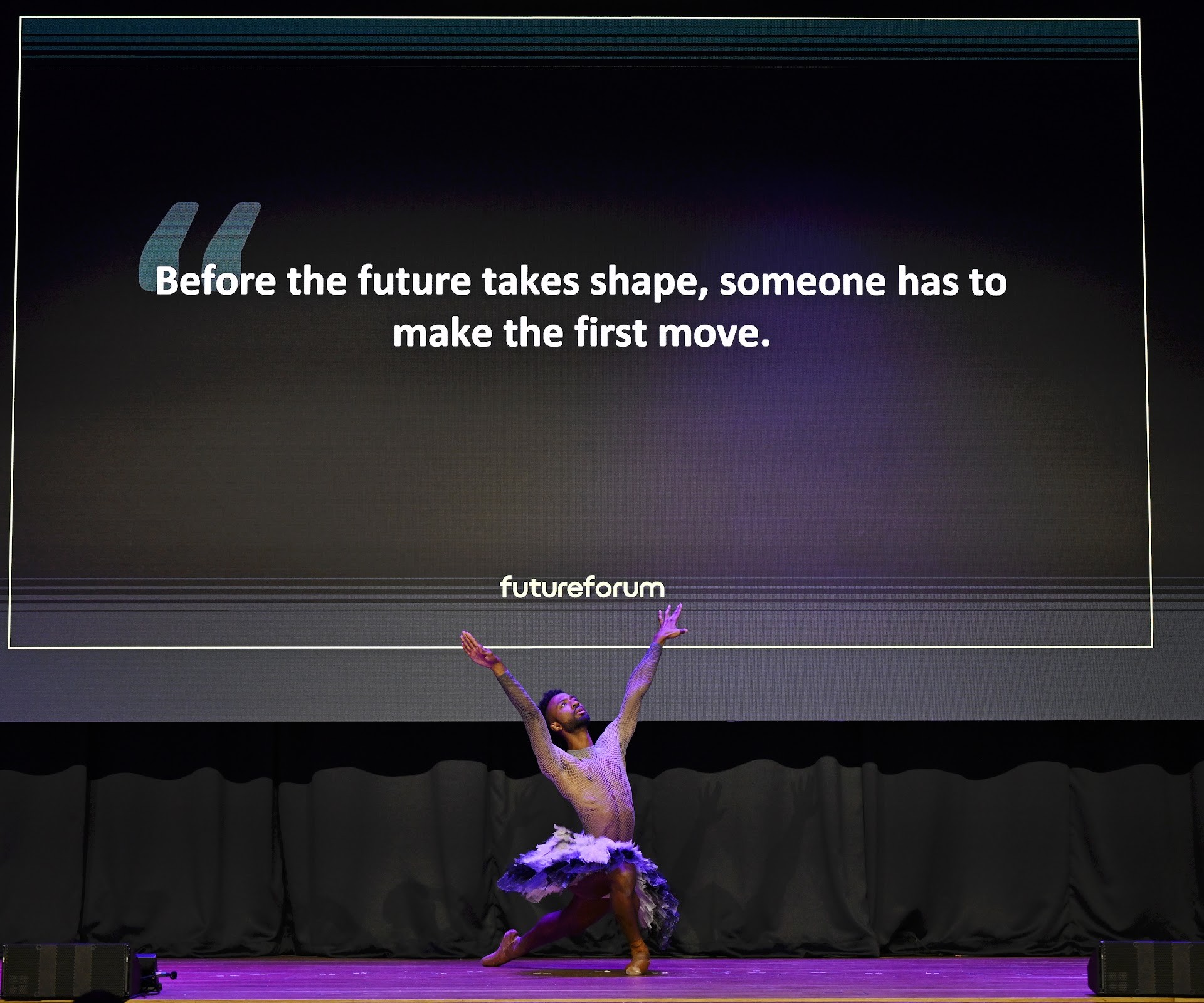 A dancer performs beneath a screen reading: Before the future takes shape, someone has to make the first move.